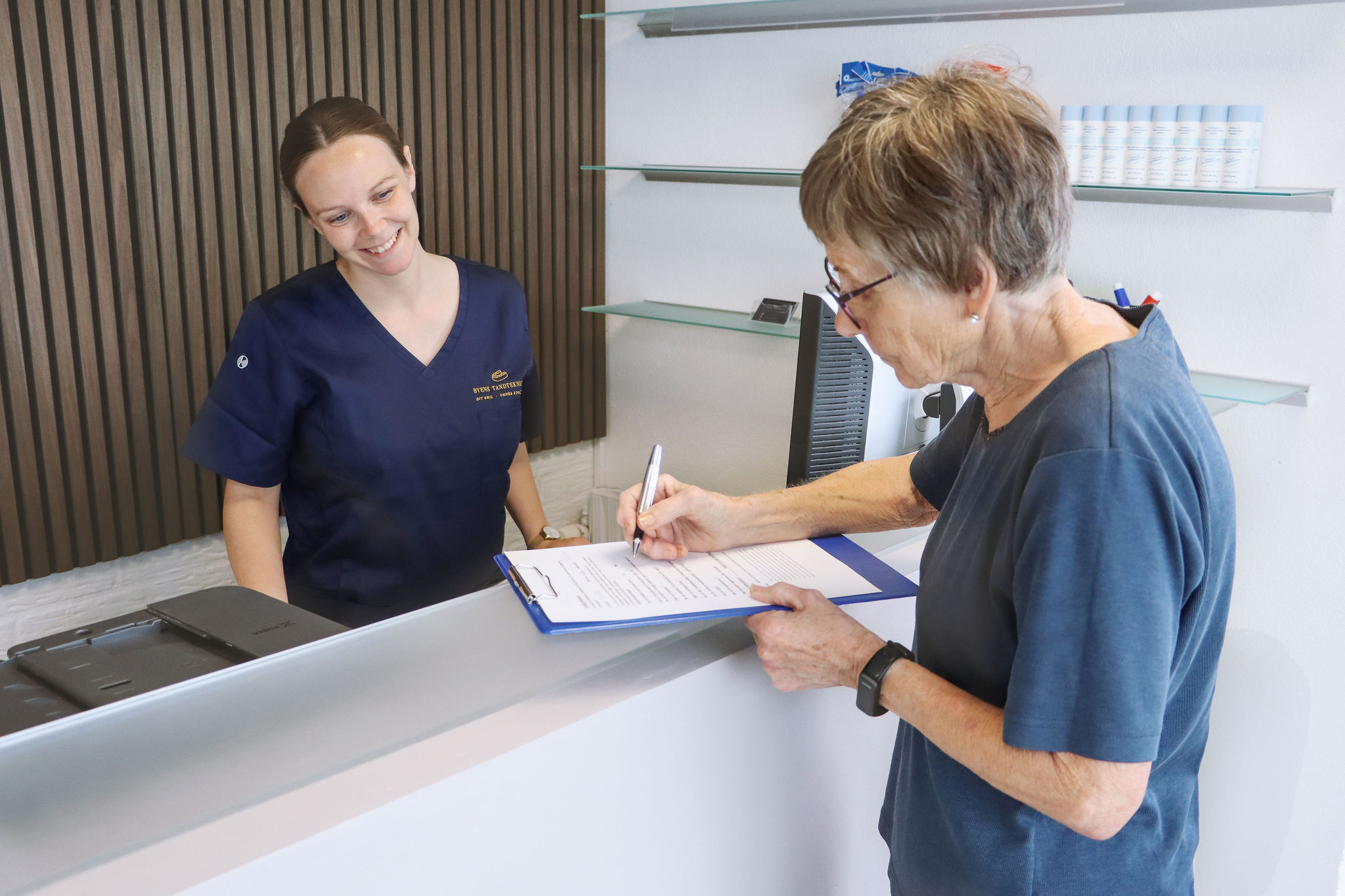 receptionist og patient er ved at udfylde velkomsseddel